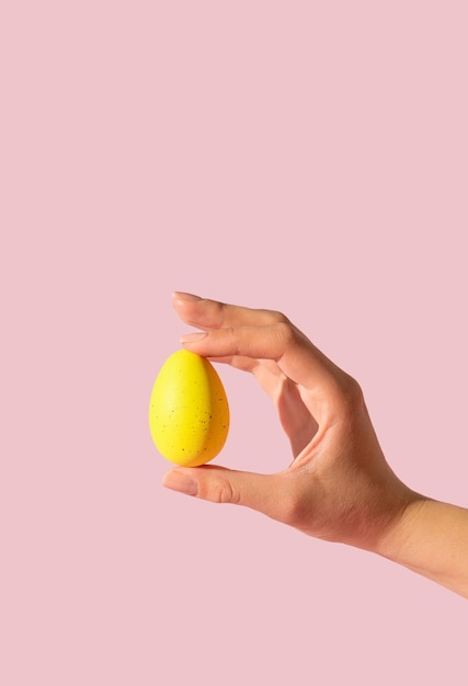 Donna mano che tiene uovo giallo su sfondo rosa Stile estetico retrò Composizione creativa di Pasqua