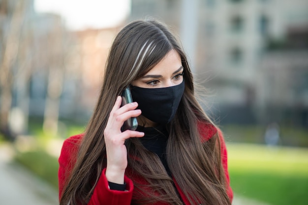 Donna mascherata che parla al telefono concetto di comunicazione covid e coronavirus