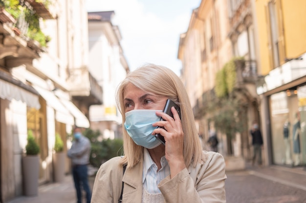 Donna mascherata che parla al telefono mentre camminava in una strada cittadina durante la pandemia di coronavirus