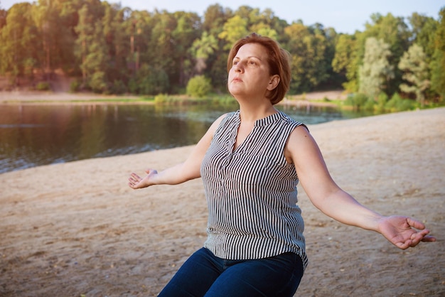 Donna matura alla spiaggia di destinazione di vacanza contemplando il lago seduto sulla riva