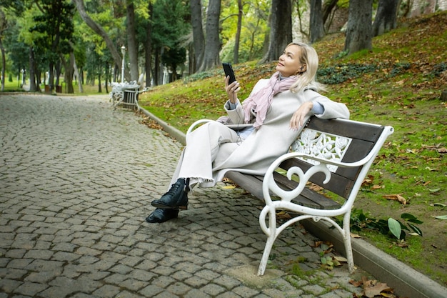 Donna matura che ascolta musica su una panchina nel parco d'autunno