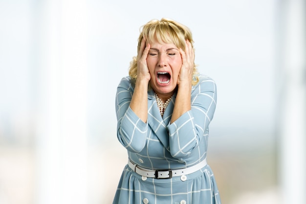 Donna matura che grida in preda alla disperazione. Immagine ravvicinata di donna stressata e scioccata che grida con espressione disperata e inorridita, le mani sulla testa.