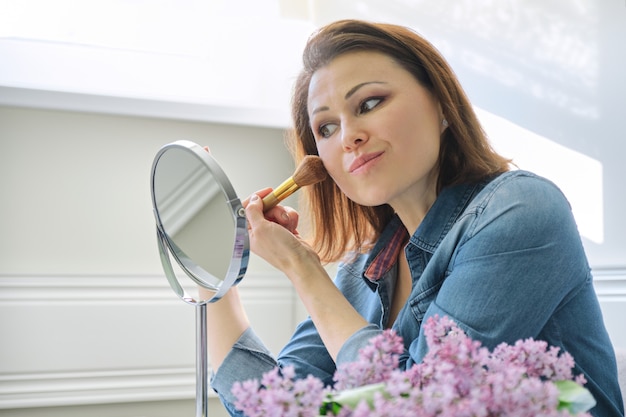 Donna matura che guarda il suo viso nello specchio, facendo il trucco