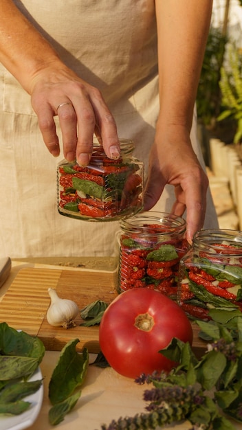 donna matura che inscatola i pomodori secchi con basilico e aglio nel cortile sul retro al tramonto