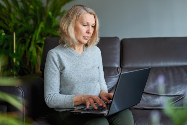 Donna matura che lavora online seduto su un divano in una casa