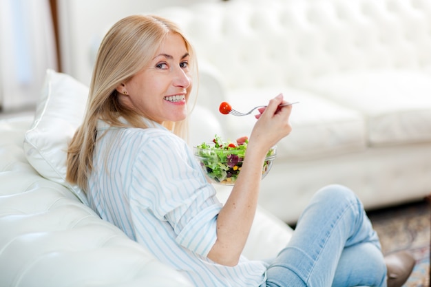 Donna matura che mangia un'insalata sana sul suo sofà