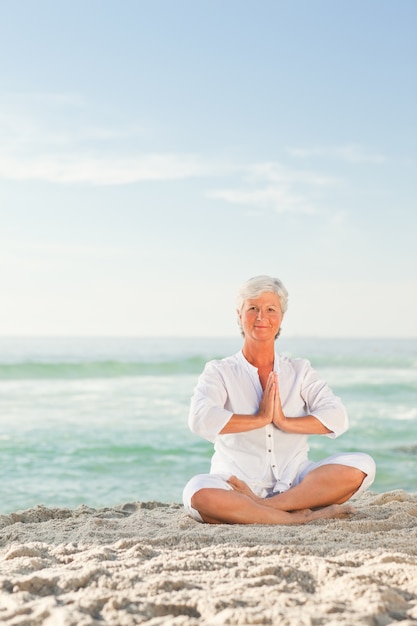 Donna matura che praticano yoga sulla spiaggia