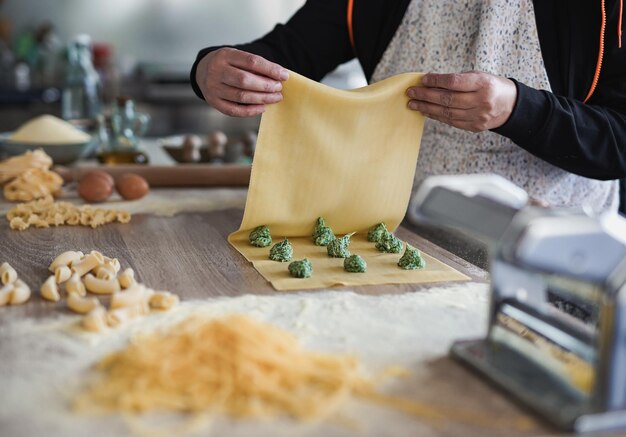 Donna matura che prepara ravioli freschi con ricotta e spinaci all'interno di un pastificio