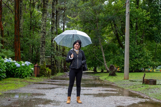 Donna matura che tiene un ombrello trasparente in mezzo alla natura in una giornata piovosa