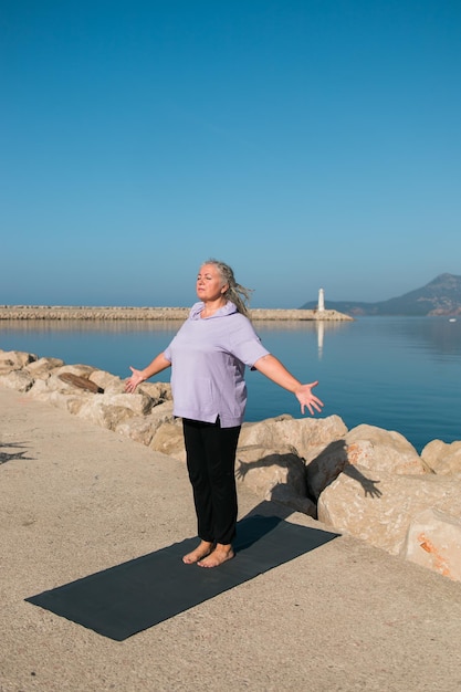 Donna matura con dreadlocks che si allena facendo esercizi di yoga sulla spiaggia del mare copia spazio benessere benessere e concetto di età anziana attiva