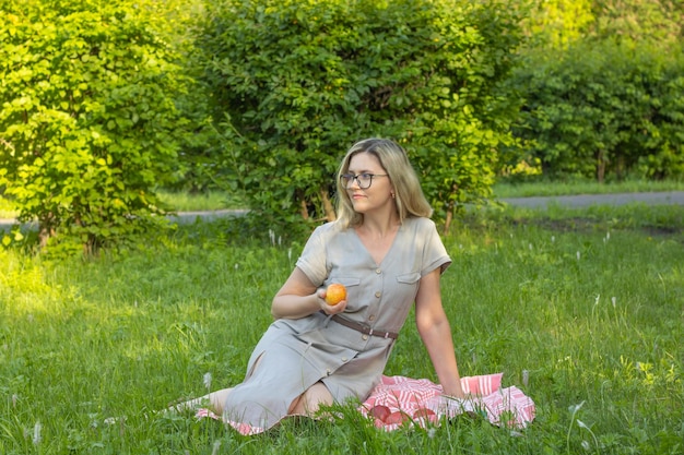 Donna matura con gli occhiali sta riposando nel parco Mangiare una mela su un prato verde all'ombra