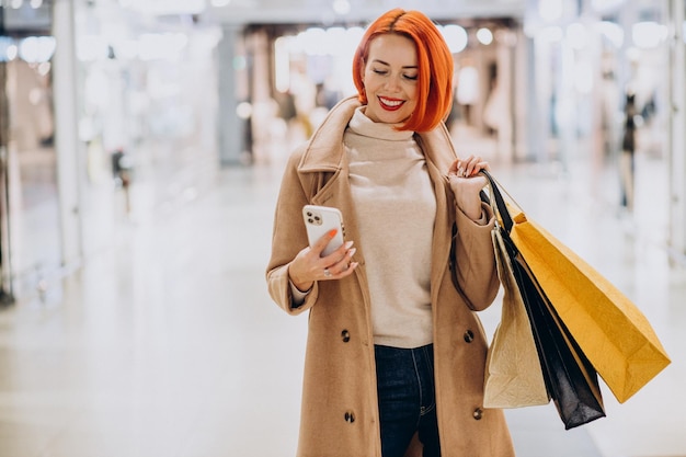 Donna matura con le borse della spesa nel centro commerciale usando il telefono