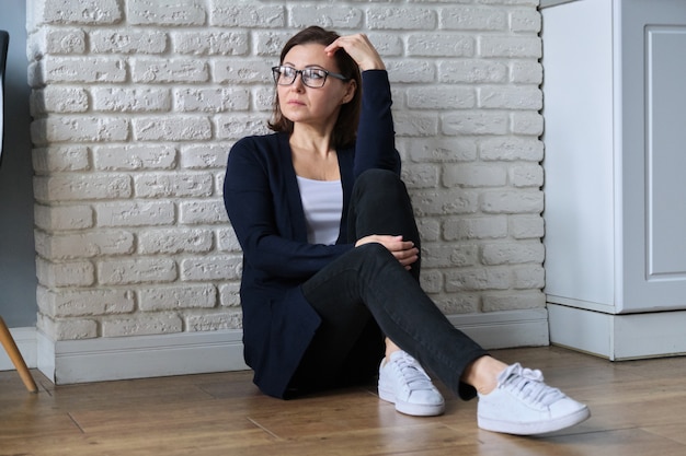 Donna matura depressa che si siede sul pavimento a casa