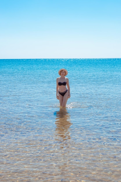 Donna matura e snella in costume da bagno esce dall'acqua in una giornata di sole Vacanze estive al mare