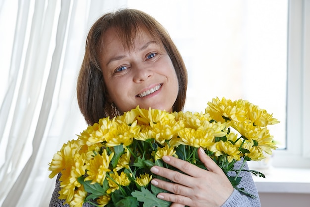 Donna matura felice che tiene una bracciata di fiori gialli