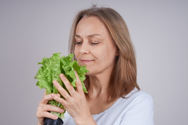 Donna matura in una camicia bianca che tiene un mazzo di insalata verde