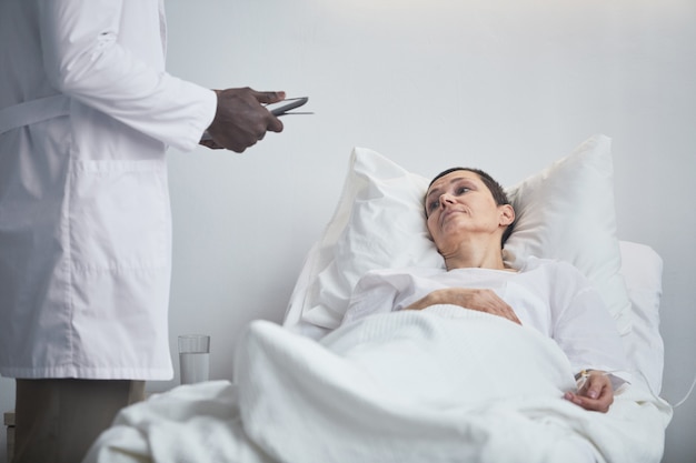 Donna matura sdraiata sul letto e parlando con il dottore in ospedale