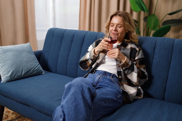 Donna matura soddisfatta che sente l'odore di un bicchiere di vino rosso a casa