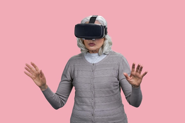 Donna matura sorpresa che indossa occhiali per realtà virtuale in piedi su sfondo rosa anziani e moder