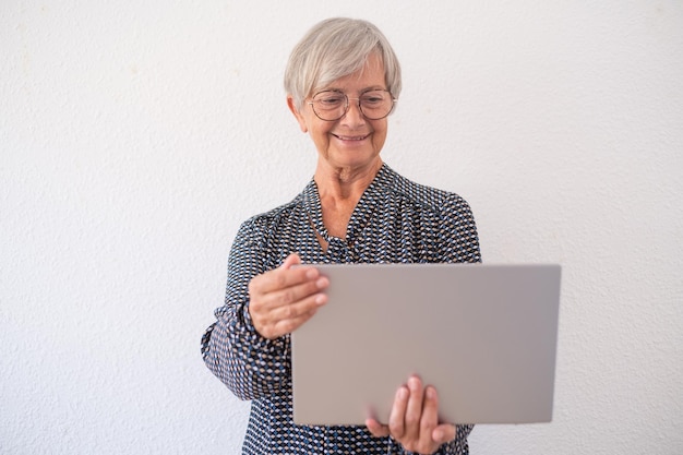 Donna matura sorridente in camicia isolata su fondo bianco che tiene il computer portatile sulle sue mani