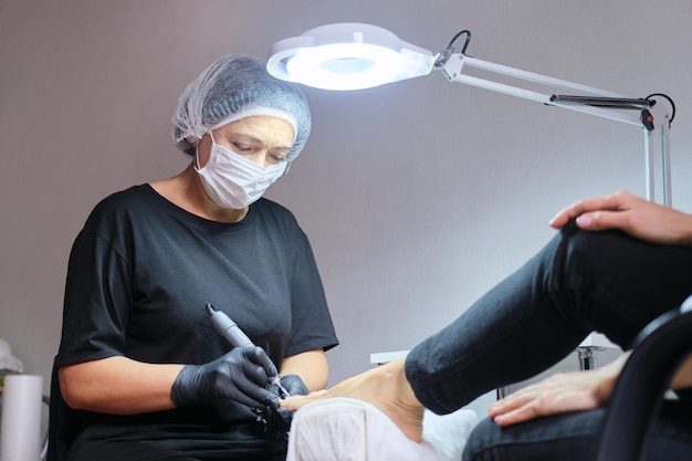 Donna matura sulla procedura di pedicure nel salone di bellezza, estetista femminile dipinge le unghie, esegue procedure termali, massaggio ai piedi