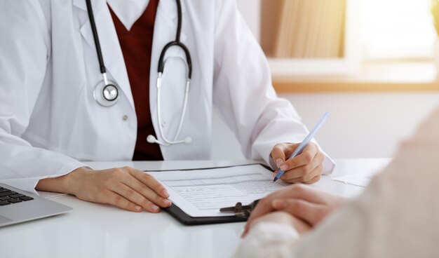 Donna-medico sconosciuta che compila un modulo di domanda mentre consulta il paziente. in camera soleggiata Concetto di medicina.