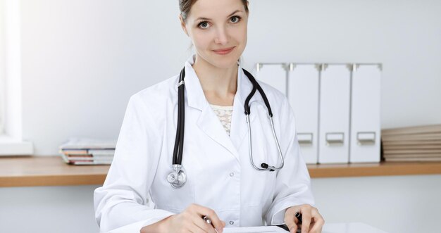 Donna-medico seduto e al lavoro presso l'ufficio della clinica soleggiata. Ritratto di medico femminile.