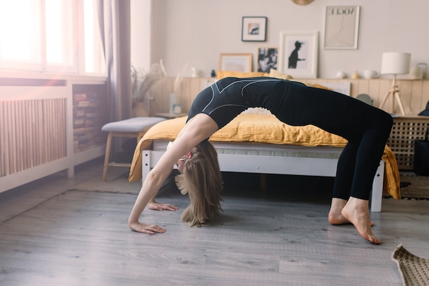 Donna meditante che indossa una maschera medica per proteggersi dal virus corona, posizione yoga sul tappetino a casa