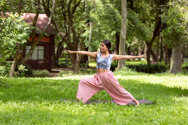 Donna messicana che fa yoga con diverse posizioni nel parco all'aperto con erba e alberi