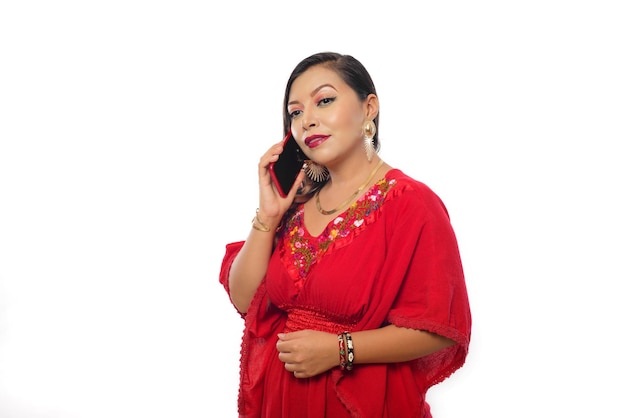 Donna messicana che indossa una camicetta rossa ricamata a mano che fa telefonata. Sfondo bianco.