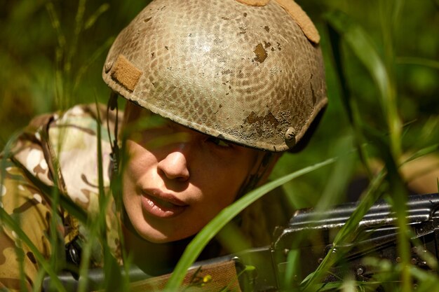 Donna militare caucasica in equipaggiamento tattico in posa per una foto durante la stagione estiva Indossando uniforme mimetica verde e fucile d'assalto in equipaggiamento militare e auricolare la signora sta guardando di lato