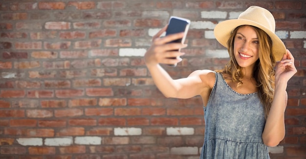 Donna millenaria in abiti estivi che si fa selfie contro il muro di mattoni rossi