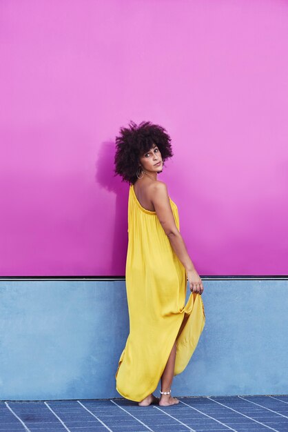 Donna mulatta dai capelli afro in un vestito giallo e sfondo viola.