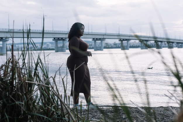 Donna multirazziale afroamericana sorridente dai capelli neri ricci che passeggia sul lago di fiume Femmina di razza mista in spiaggia