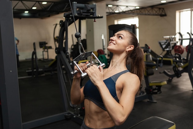 Donna muscolare atletica che esercita la schiena in macchina per esercizi lat con presa stretta in palestra