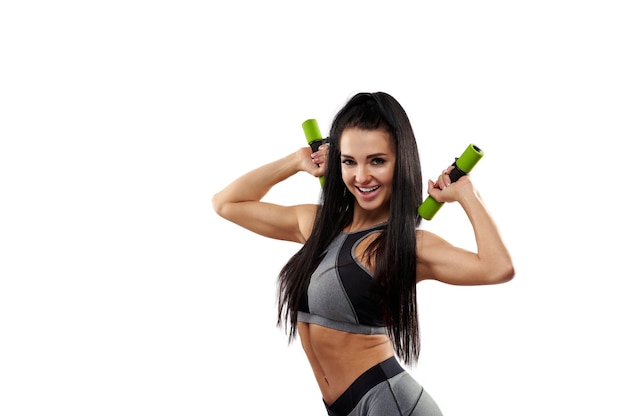 Donna muscolare in abbigliamento sportivo grigio e manubri nelle mani in posa e sorridente mentre pompano muscoli della spalla e bicipiti