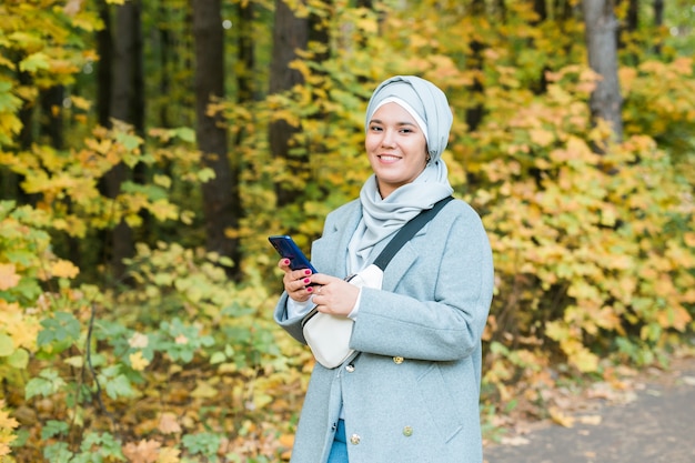 Donna musulmana al parco che utilizza smartphone connesso wireless online