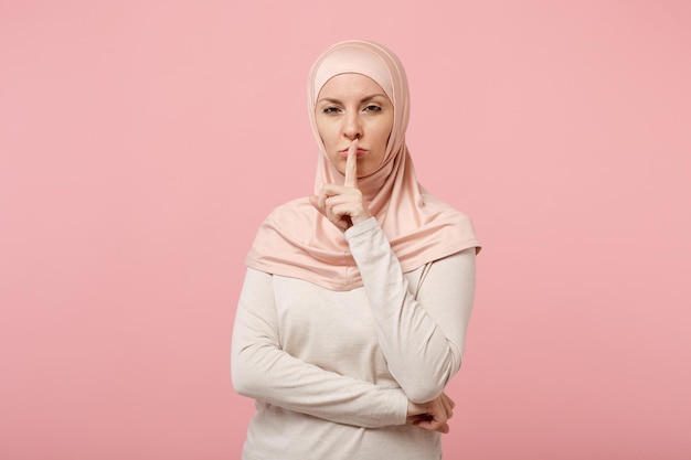 Donna musulmana araba in abiti leggeri hijab in posa isolata su sfondo rosa. Concetto di stile di vita dell'Islam religioso della gente. Mock up spazio di copia. Dire silenzio stai zitto con il dito sulle labbra shhh gesto.