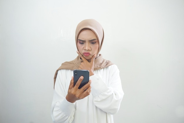 Donna musulmana asiatica arrabbiata che mostra il telefono cellulare isolato su sfondo bianco