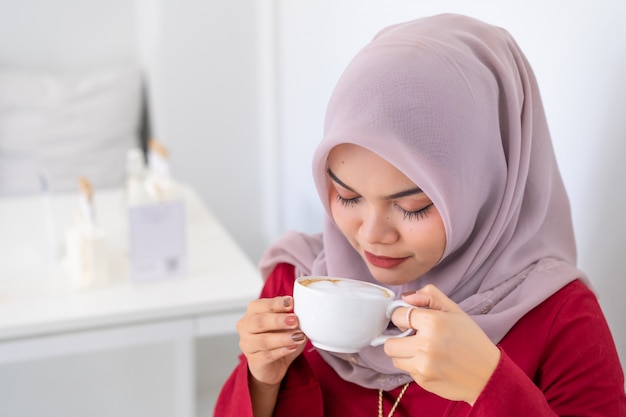 Donna musulmana asiatica moderna felice di affari che lavora al caffè sentente l'odore dello scrittorio.