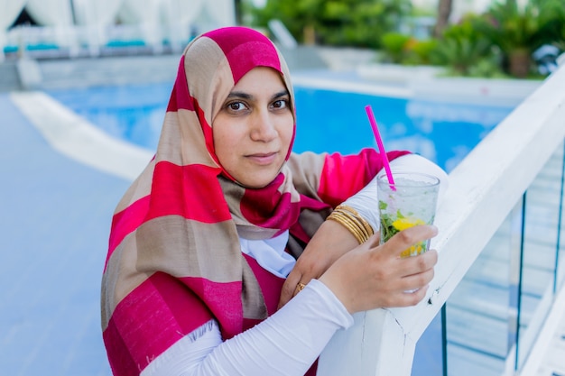 donna musulmana che beve succo accanto alla piscina