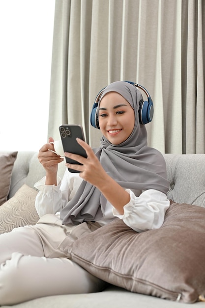 Donna musulmana che indossa hijab e cuffie che ascolta la musica mentre sorseggia un caffè