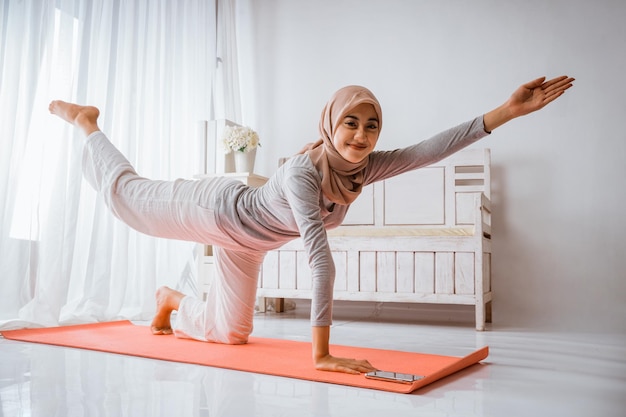 Donna musulmana che indossa pantaloni tshirt hijab sorridendo riscaldandosi prima dell'esercizio facendo yoga o pilates pos