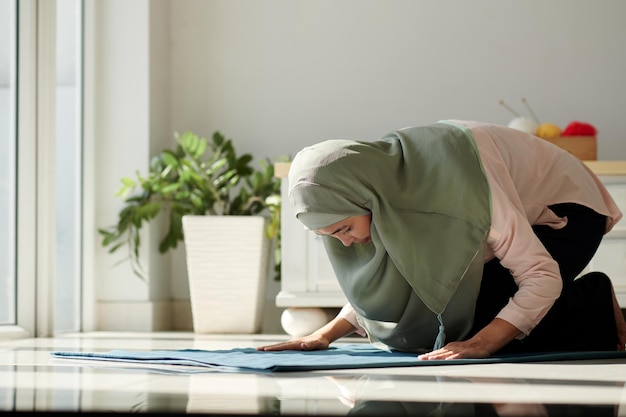 Donna musulmana che prega su un piccolo tappeto a casa