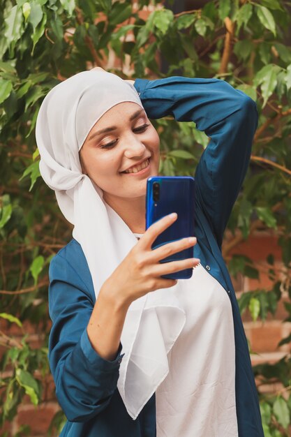 Donna musulmana che si fa selfie felice e bella ragazza con sciarpa si fa una foto usando lo smartphone