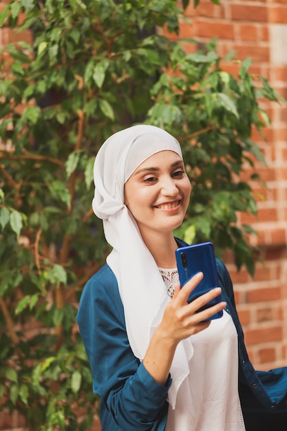 Donna musulmana che si fa selfie felice e bella ragazza con sciarpa si fa una foto usando lo smartphone