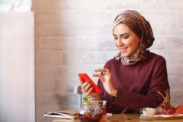 Donna musulmana che si siede nel caffè utilizzando il telefono per la corrispondenza