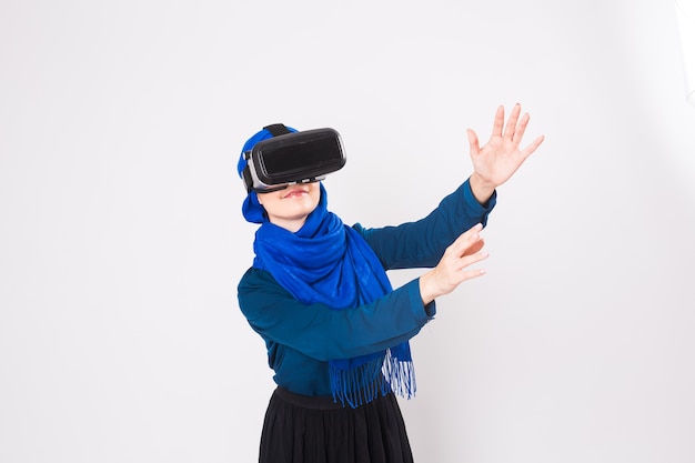 Donna musulmana con occhiali per realtà virtuale. Studio girato, sfondo bianco.