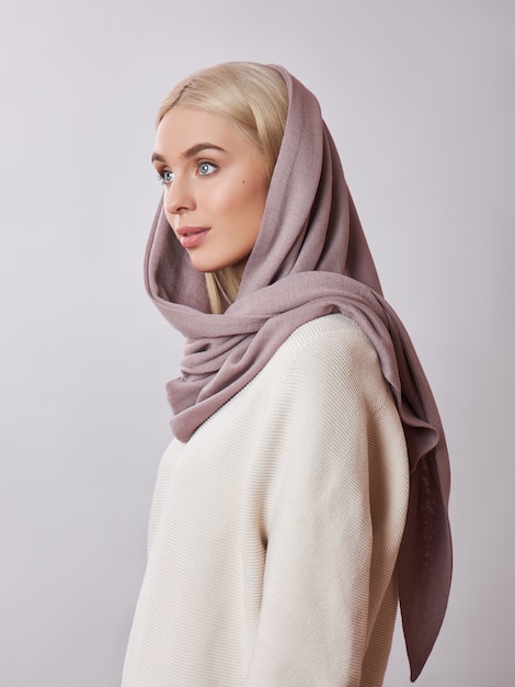 Donna musulmana europea con i capelli biondi in uno scialle di foulard vestito in testa. Bella ragazza in maglione con pelle morbida, cosmetici naturali