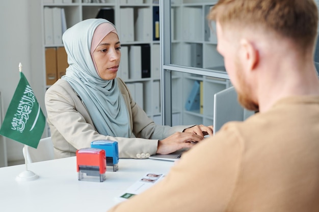Donna musulmana moderna che lavora nell'ambasciata dell'Arabia Saudita che consulta un uomo irriconoscibile per la domanda di visto